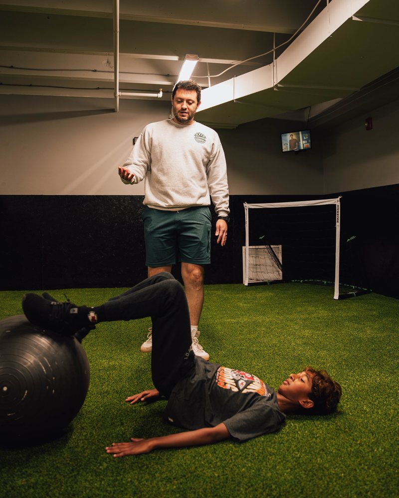 A young player doing a stability ball exercise while a Prestige trainer coaches him